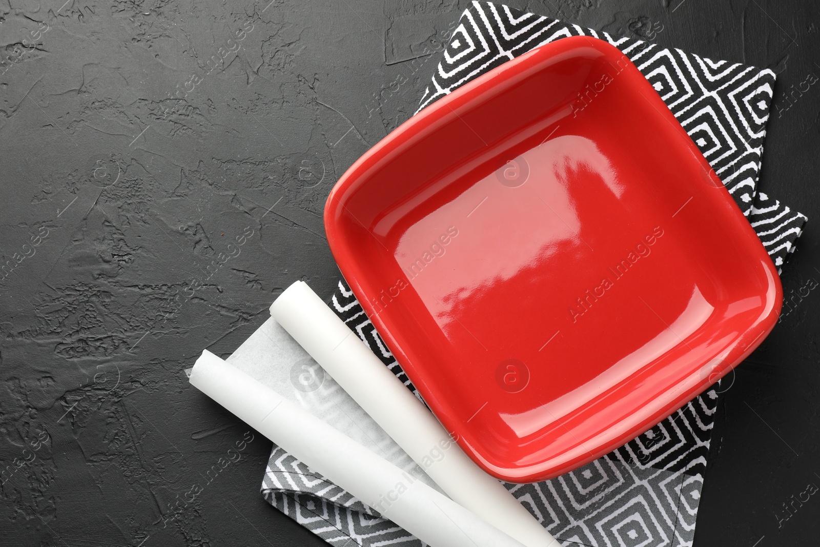 Photo of Red ceramic casserole and baking parchment paper on black table, top view. Space for text