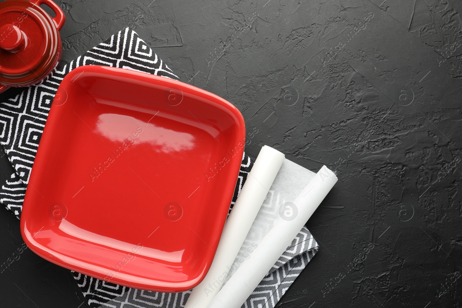 Photo of Red ceramic casseroles and baking parchment paper on black table, flat lay. Space for text