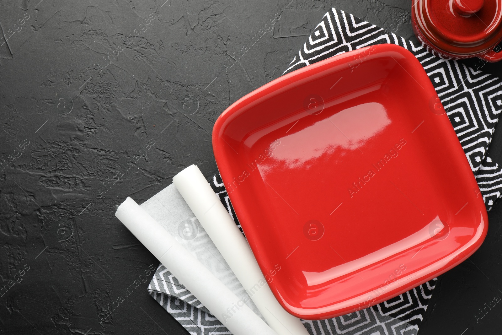 Photo of Red ceramic casseroles and baking parchment paper on black table, flat lay. Space for text