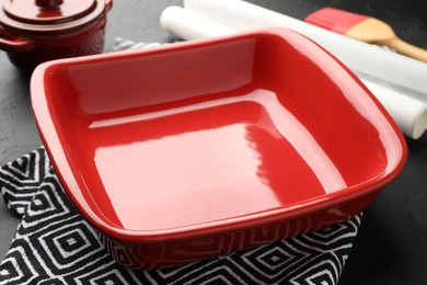 Photo of Red ceramic casseroles, baking parchment paper and brush on black table, closeup