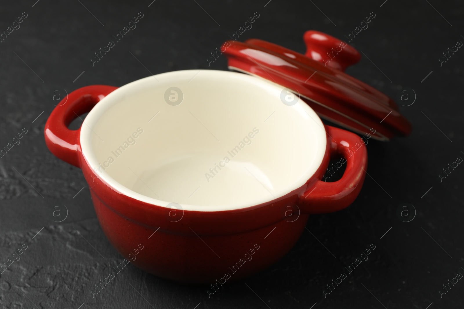 Photo of Red ceramic casserole and lid on black table, closeup