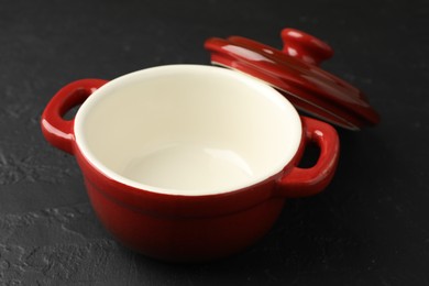 Photo of Red ceramic casserole and lid on black table, closeup