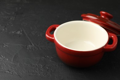 Photo of Red ceramic casserole and lid on black table, closeup. Space for text