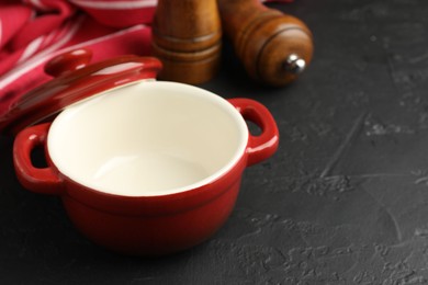 Photo of Red ceramic casserole and shakers on black table, closeup. Space for text