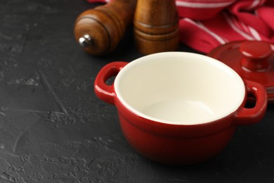 Photo of Red ceramic casserole and shakers on black table, closeup. Space for text