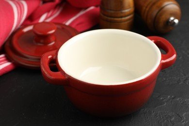 Photo of Red ceramic casserole and shakers on black table, closeup