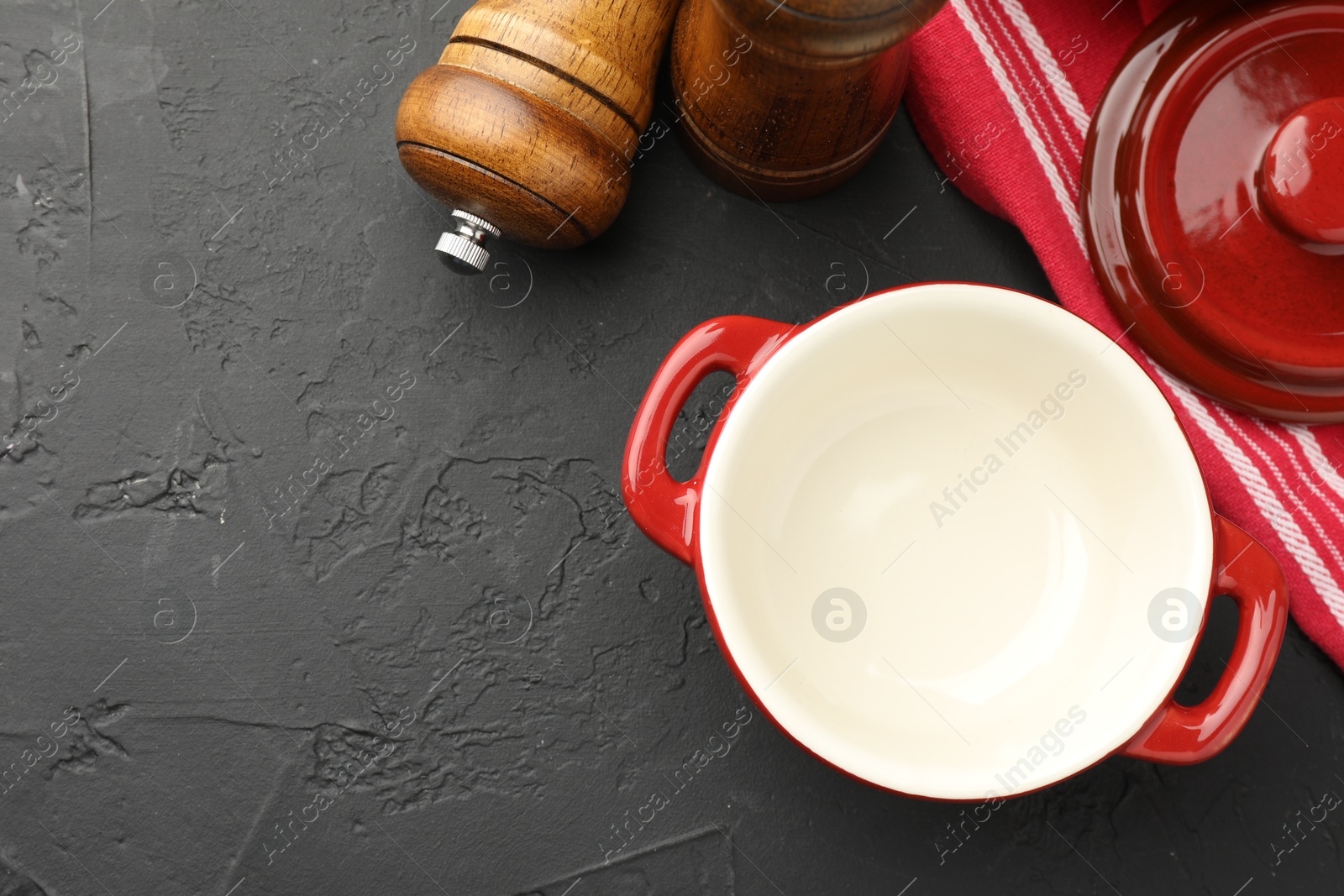 Photo of Red ceramic casserole and shakers on black table, flat lay. Space for text