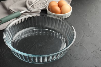 Photo of Glass casserole, whisk and eggs on black table, closeup. Space for text