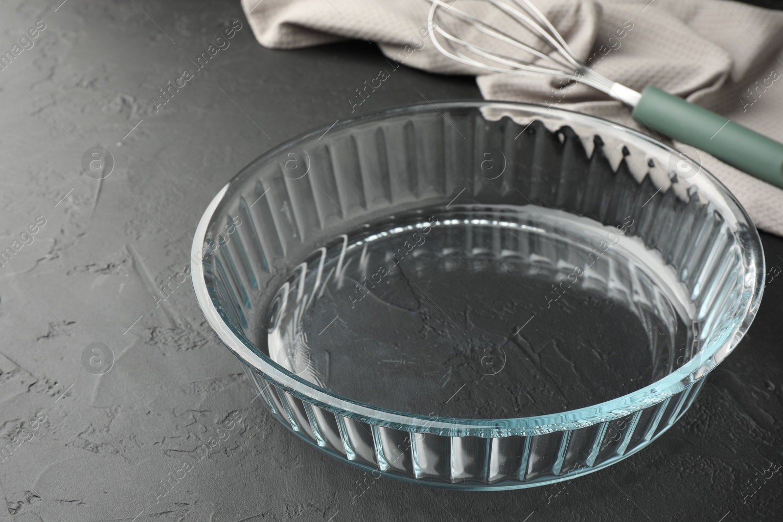 Photo of Glass casserole and whisk on black table, closeup. Space for text