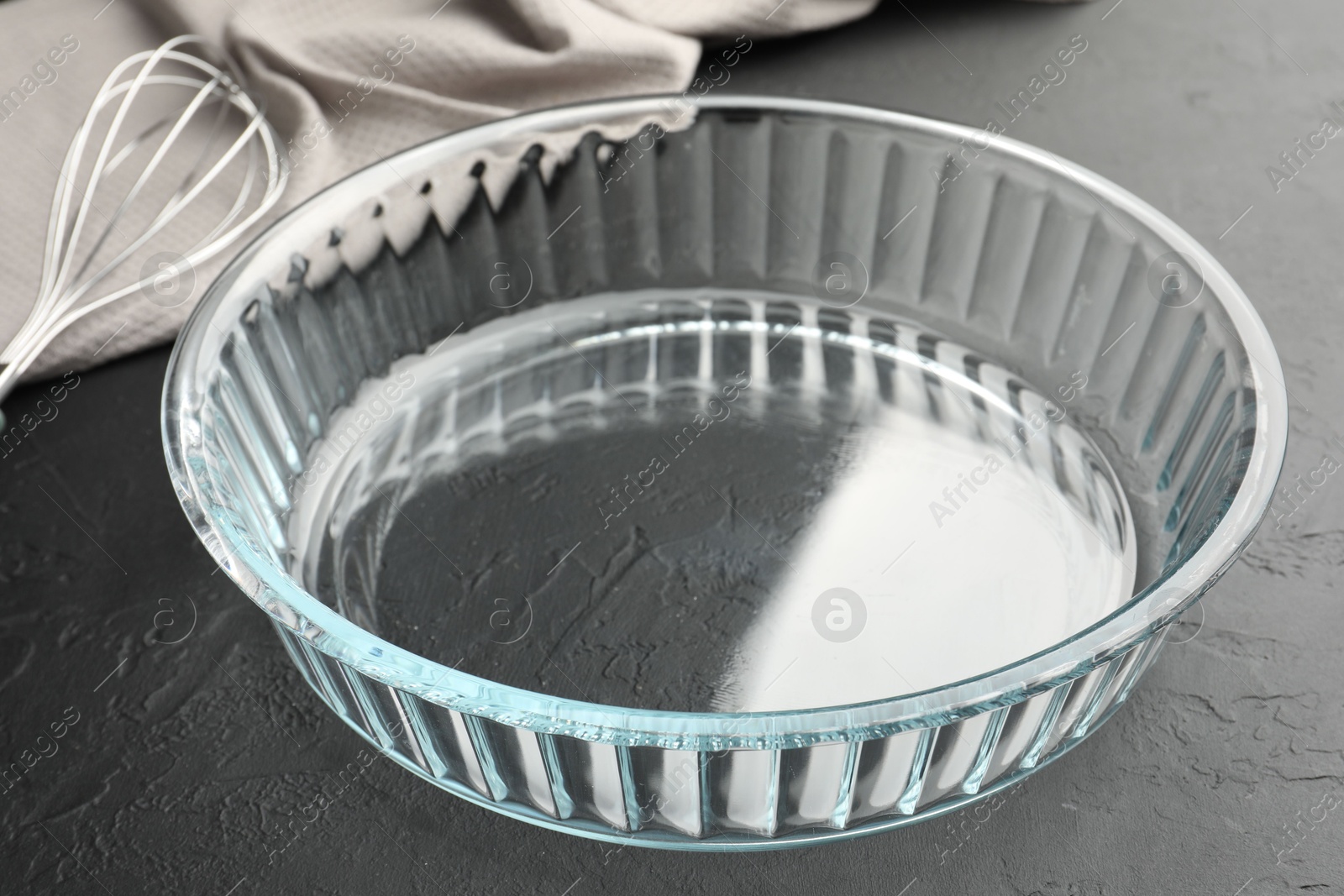 Photo of Glass casserole and whisk on black table, closeup