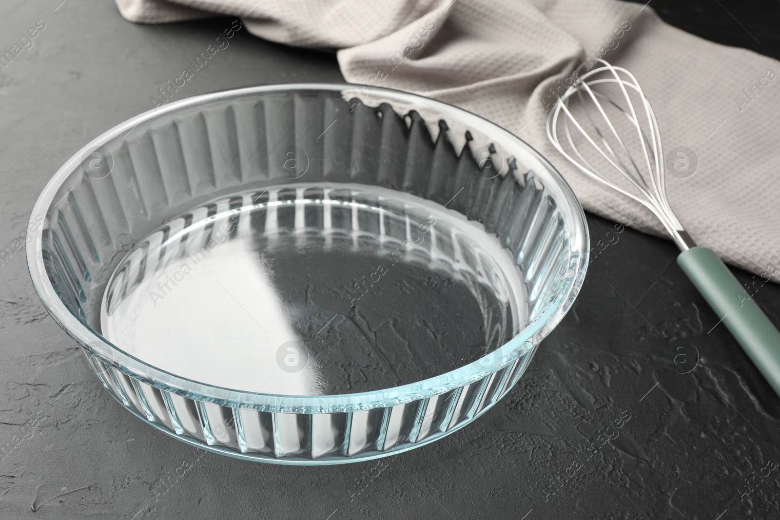 Photo of Glass casserole and whisk on black table, closeup