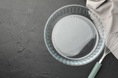 Photo of Glass casserole and whisk on black table, top view. Space for text