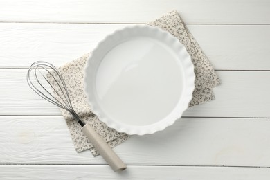 Photo of Ceramic casserole and whisk on white wooden table, top view