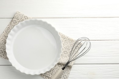 Photo of Ceramic casserole and whisk on white wooden table, top view. Space for text