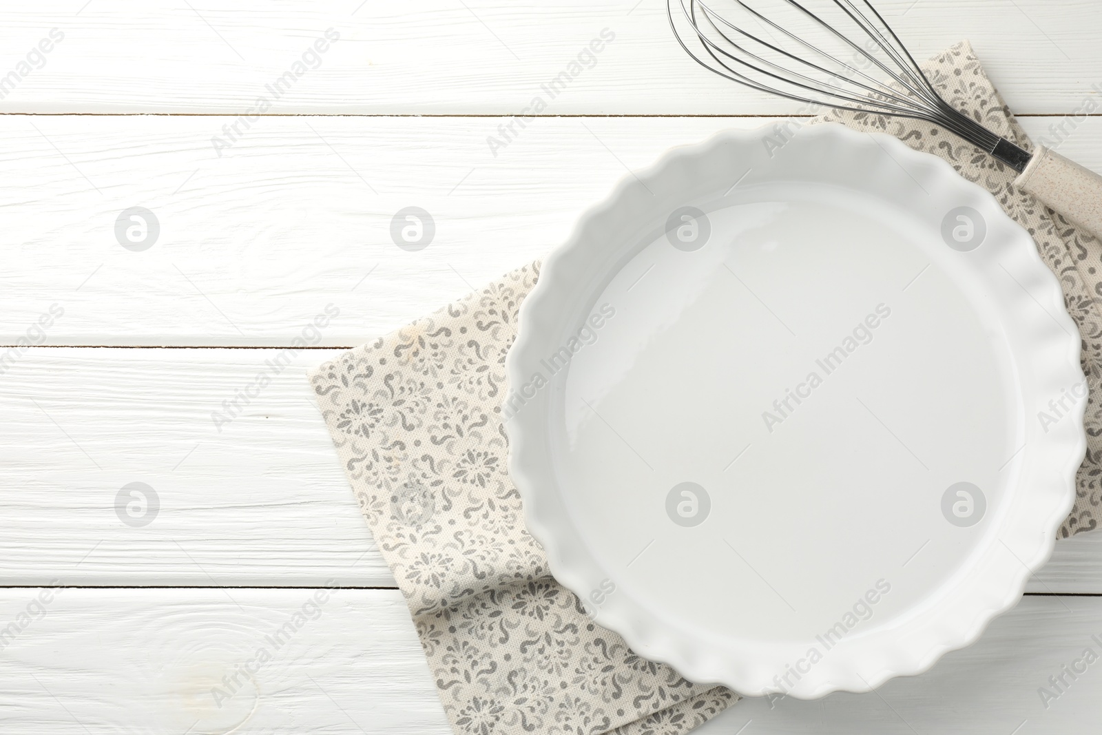 Photo of Ceramic casserole and whisk on white wooden table, top view. Space for text