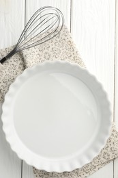 Photo of Ceramic casserole and whisk on white wooden table, top view