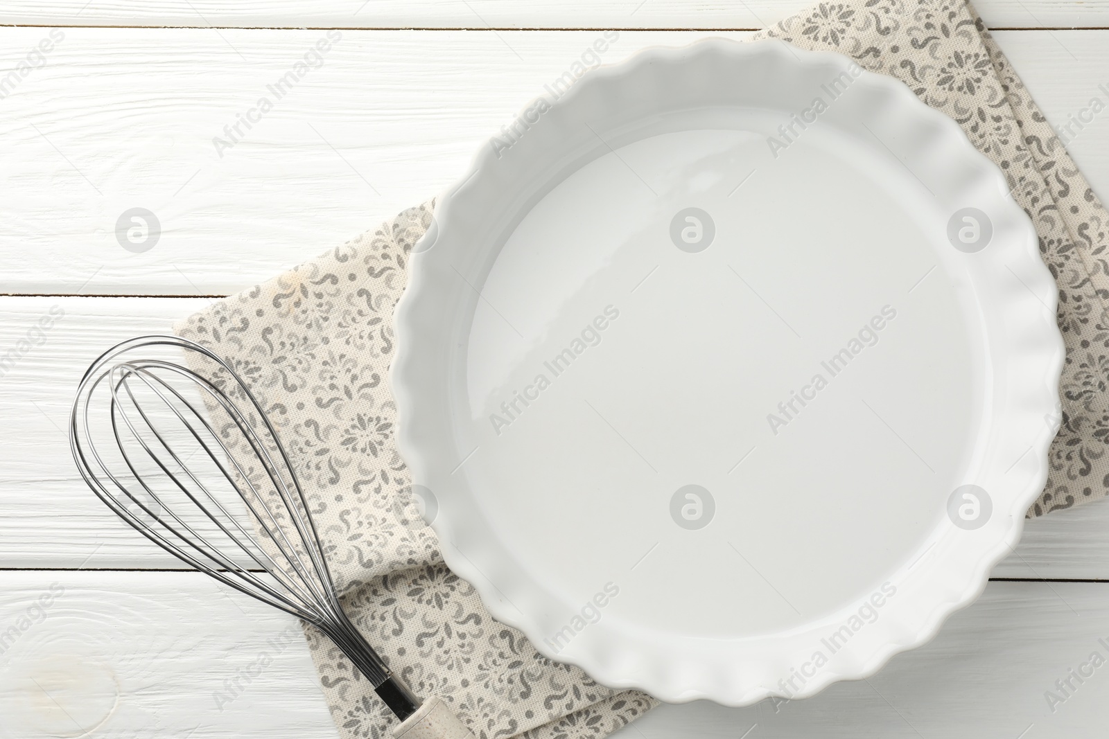 Photo of Ceramic casserole and whisk on white wooden table, top view