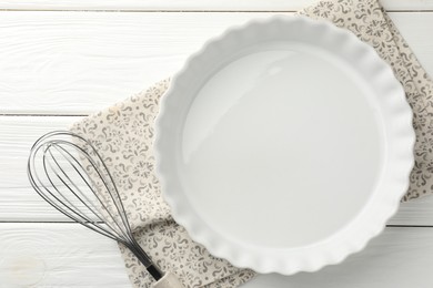 Photo of Ceramic casserole and whisk on white wooden table, top view