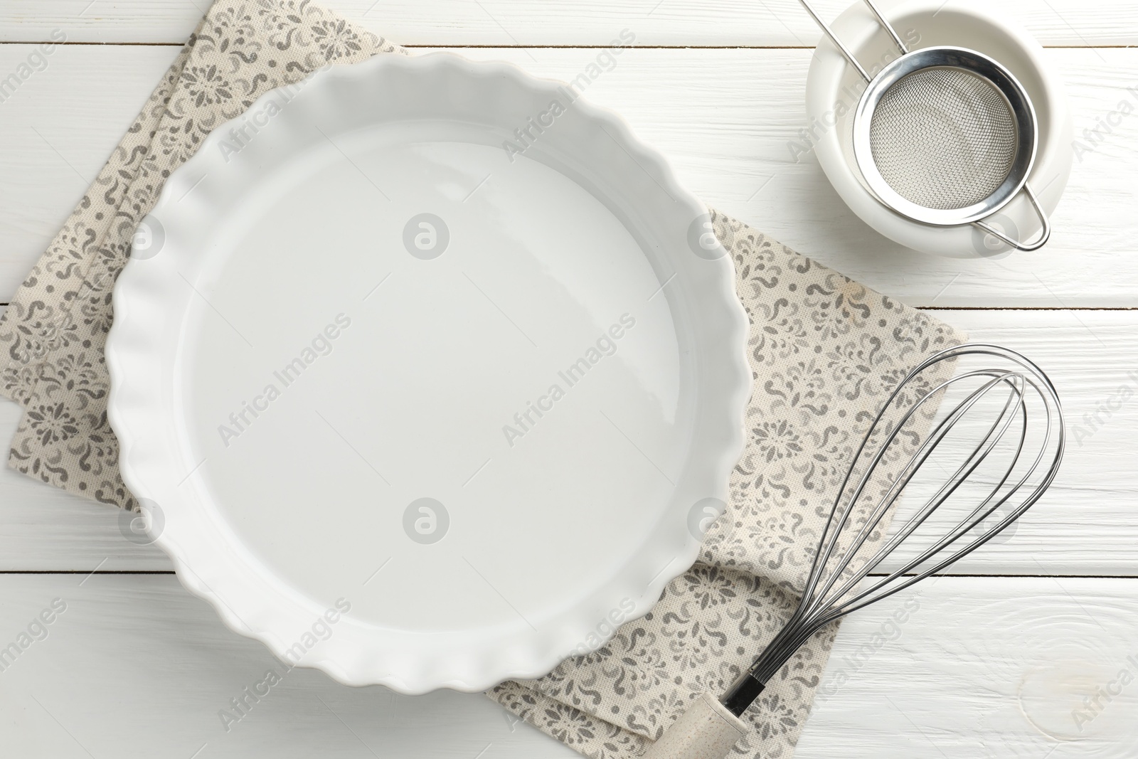 Photo of Ceramic casserole, bowl, sieve and whisk on white wooden table, flat lay