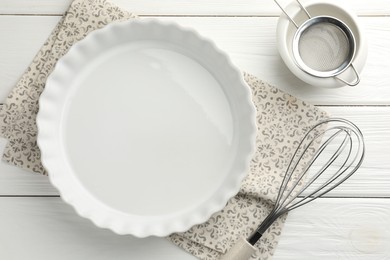 Photo of Ceramic casserole, bowl, sieve and whisk on white wooden table, flat lay