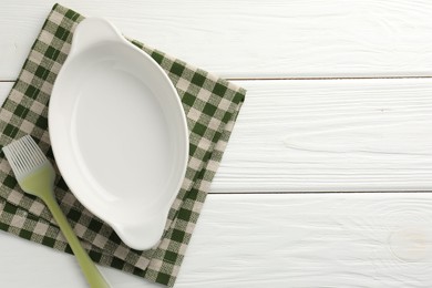 Photo of Ceramic casserole and brush on white wooden table, top view. Space for text