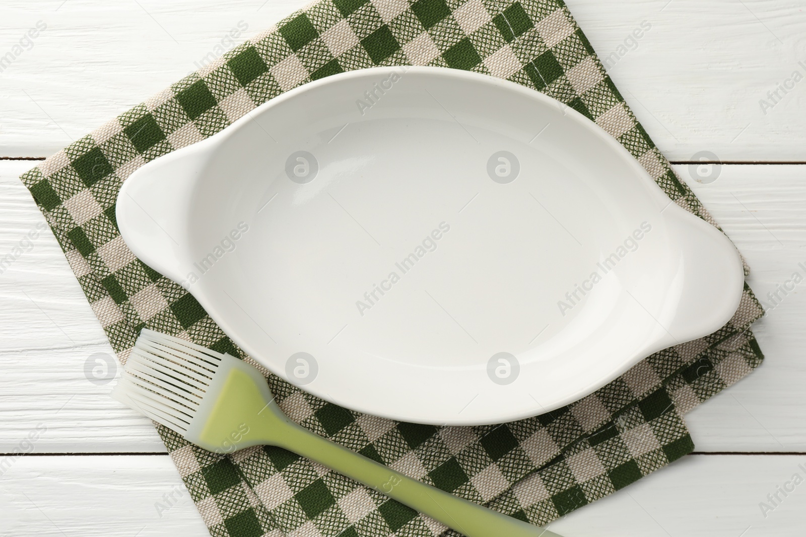 Photo of Ceramic casserole and brush on white wooden table, top view