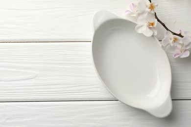 Photo of Ceramic casserole and orchid branch on white wooden table, top view. Space for text