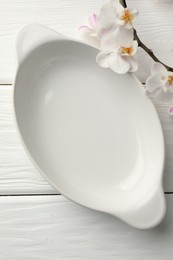 Photo of Ceramic casserole and orchid branch on white wooden table, top view