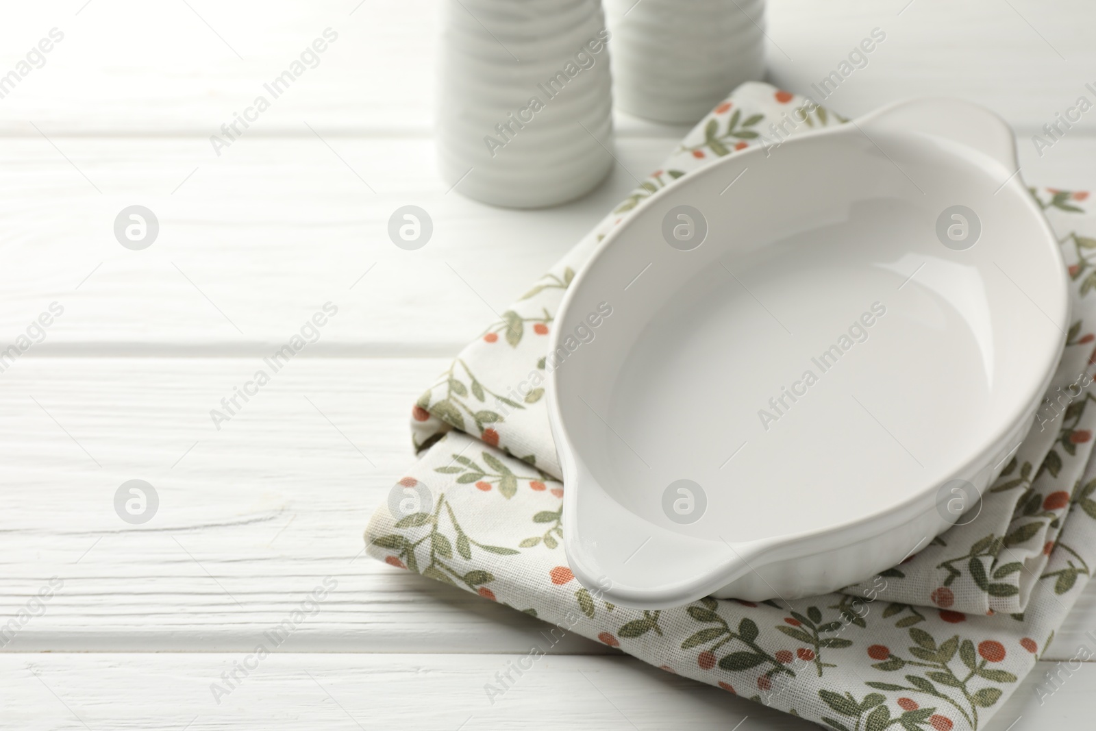 Photo of Ceramic casserole and shakers on white wooden table, closeup. Space for text