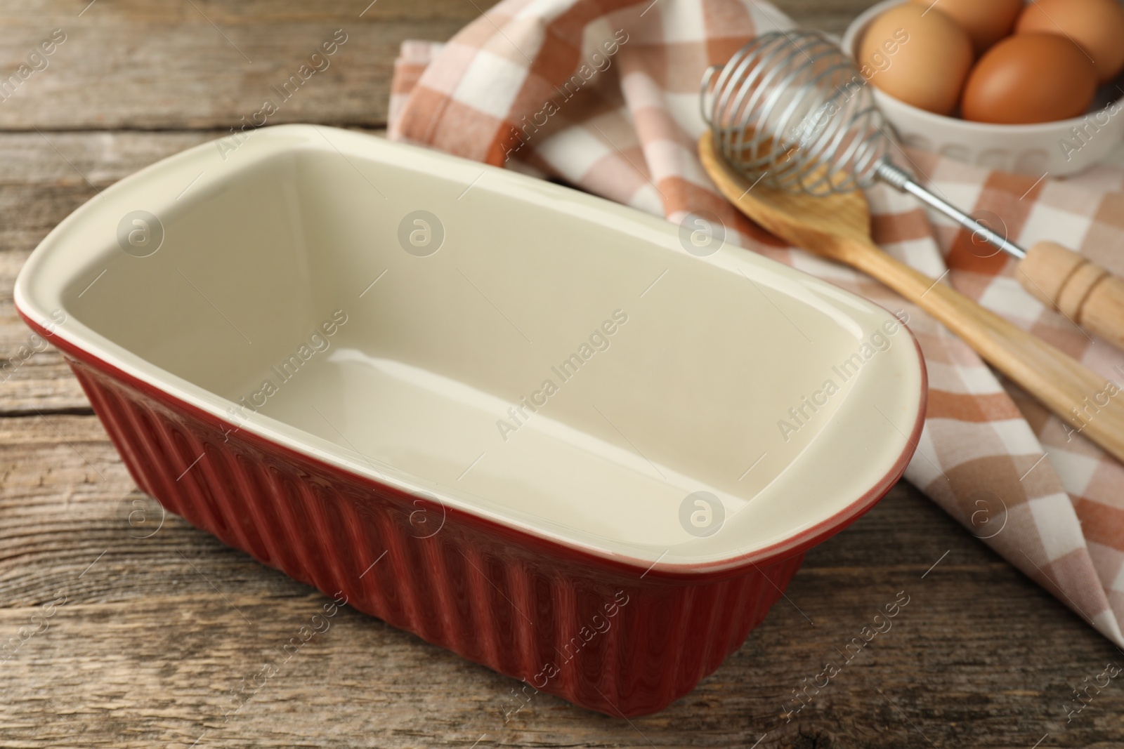 Photo of Ceramic casserole, whisk, spoon and eggs on wooden table, closeup