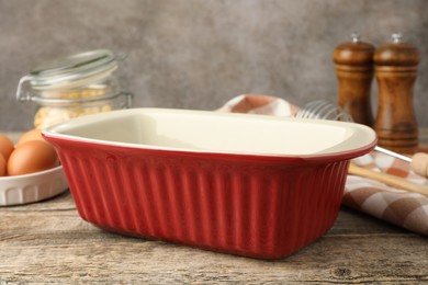 Photo of Ceramic casserole, whisk and eggs on wooden table, closeup