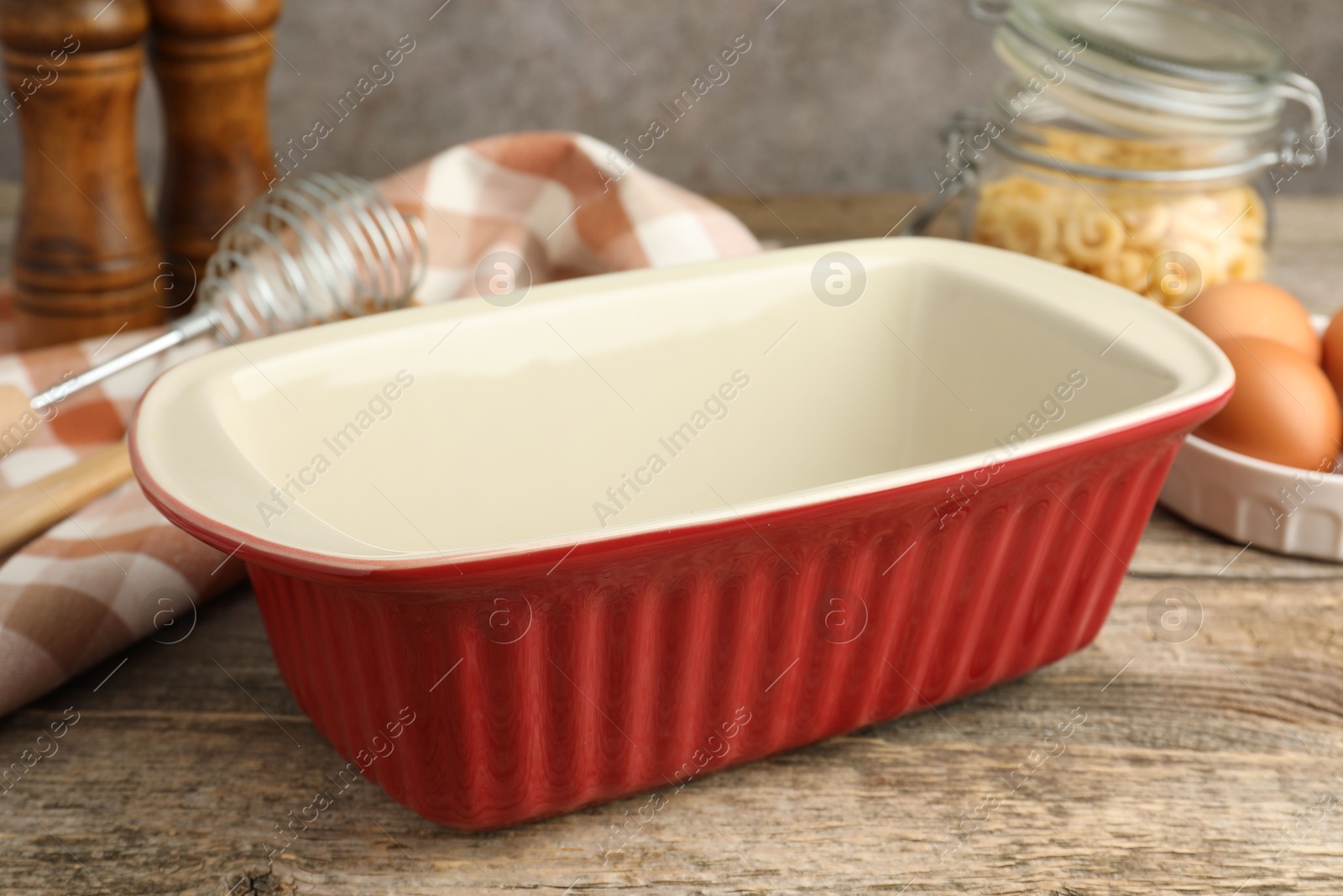 Photo of Ceramic casserole, whisk, eggs and raw pasta on wooden table, closeup