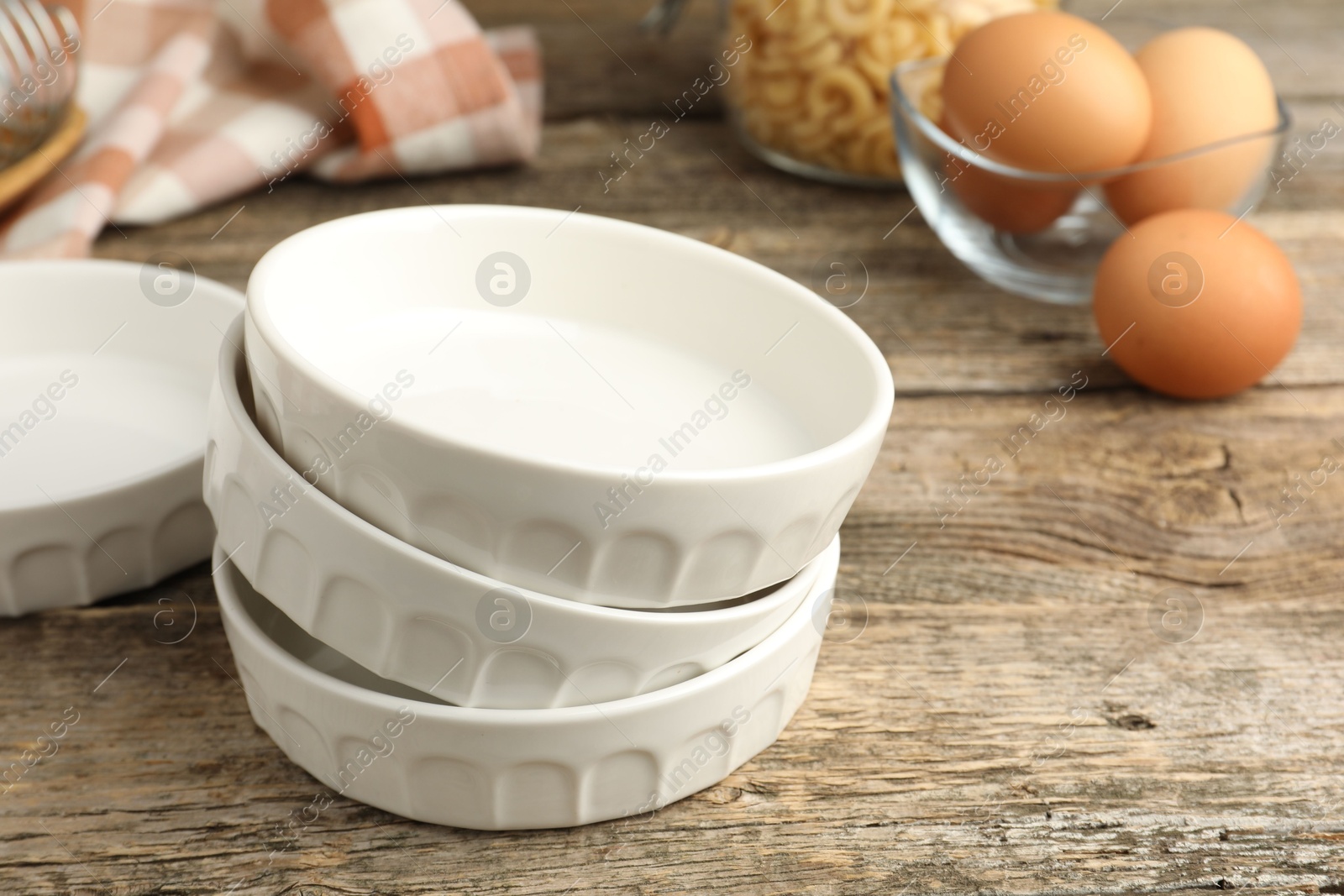 Photo of Ceramic casseroles and eggs on wooden table, closeup