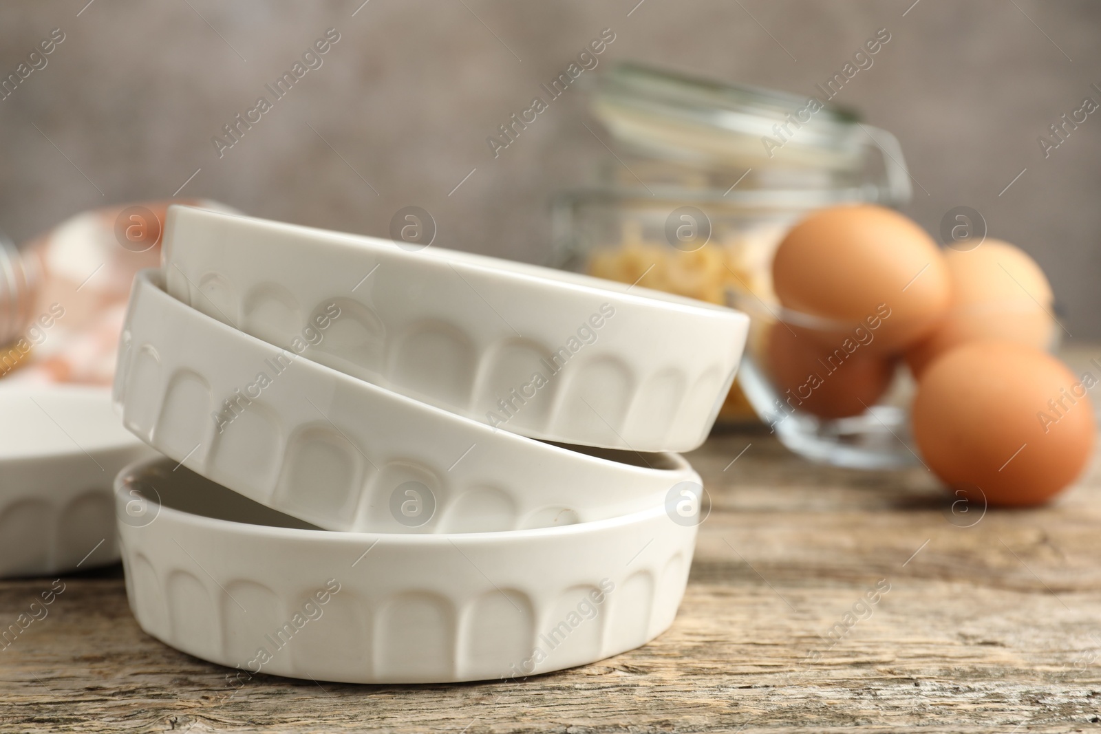 Photo of Ceramic casseroles and eggs on wooden table, closeup. Space for text