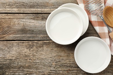 Photo of Ceramic casseroles, whisk and spoon on wooden table, flat lay. Space for text