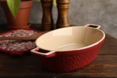 Photo of Ceramic casserole, potholder and shakers on wooden table, closeup