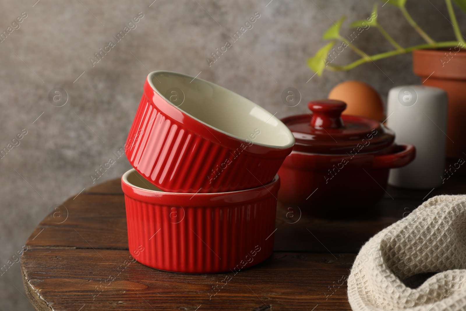 Photo of Red ceramic casseroles on wooden table. Cooking utensil