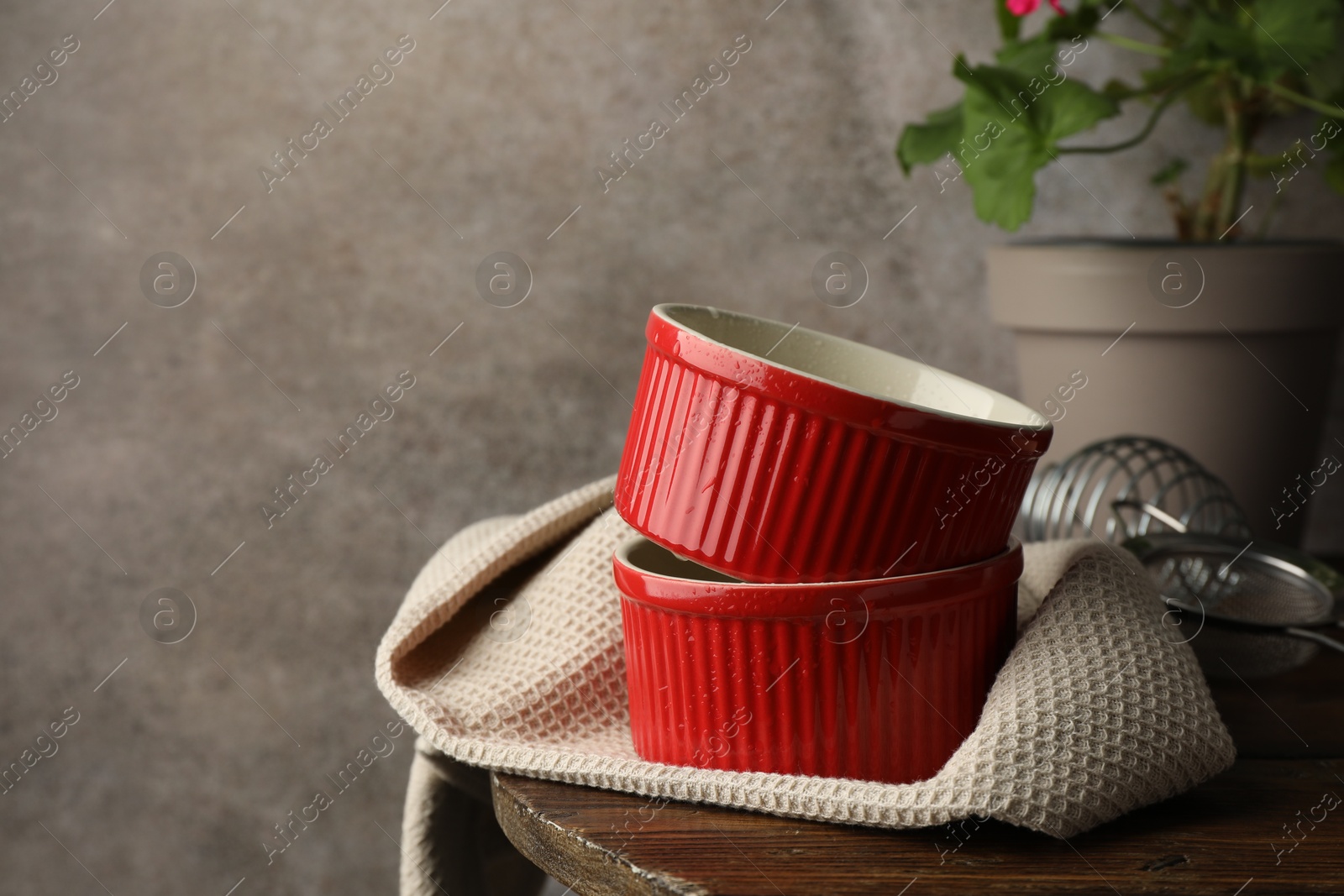 Photo of Red ceramic casseroles, sieve and whisk on wooden table, space for text