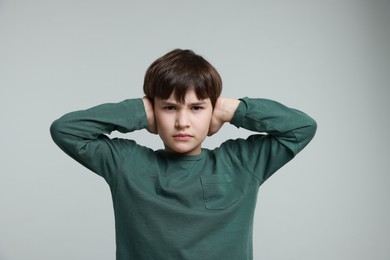 Photo of Annoyed boy covering his ears due to loud sound on grey background