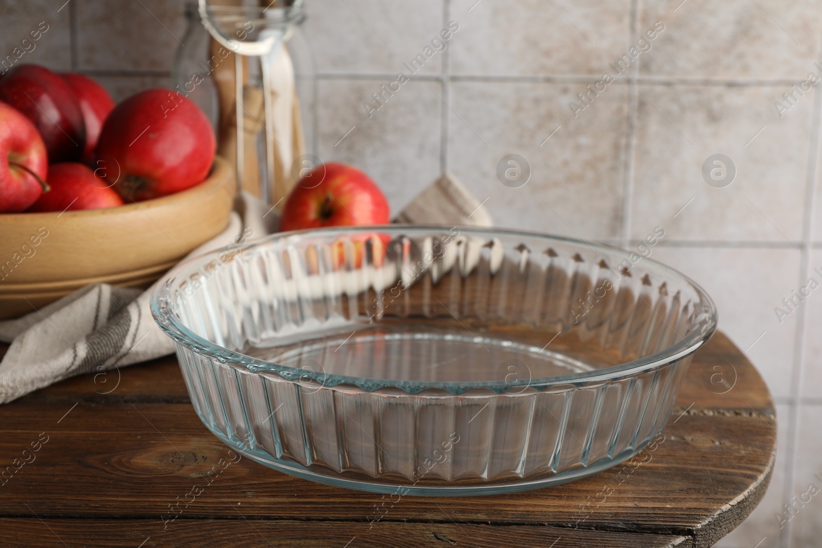 Photo of Glass casserole and apples on wooden table, closeup