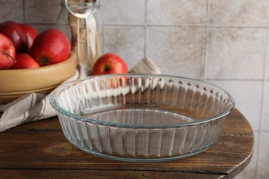 Photo of Glass casserole and apples on wooden table, closeup