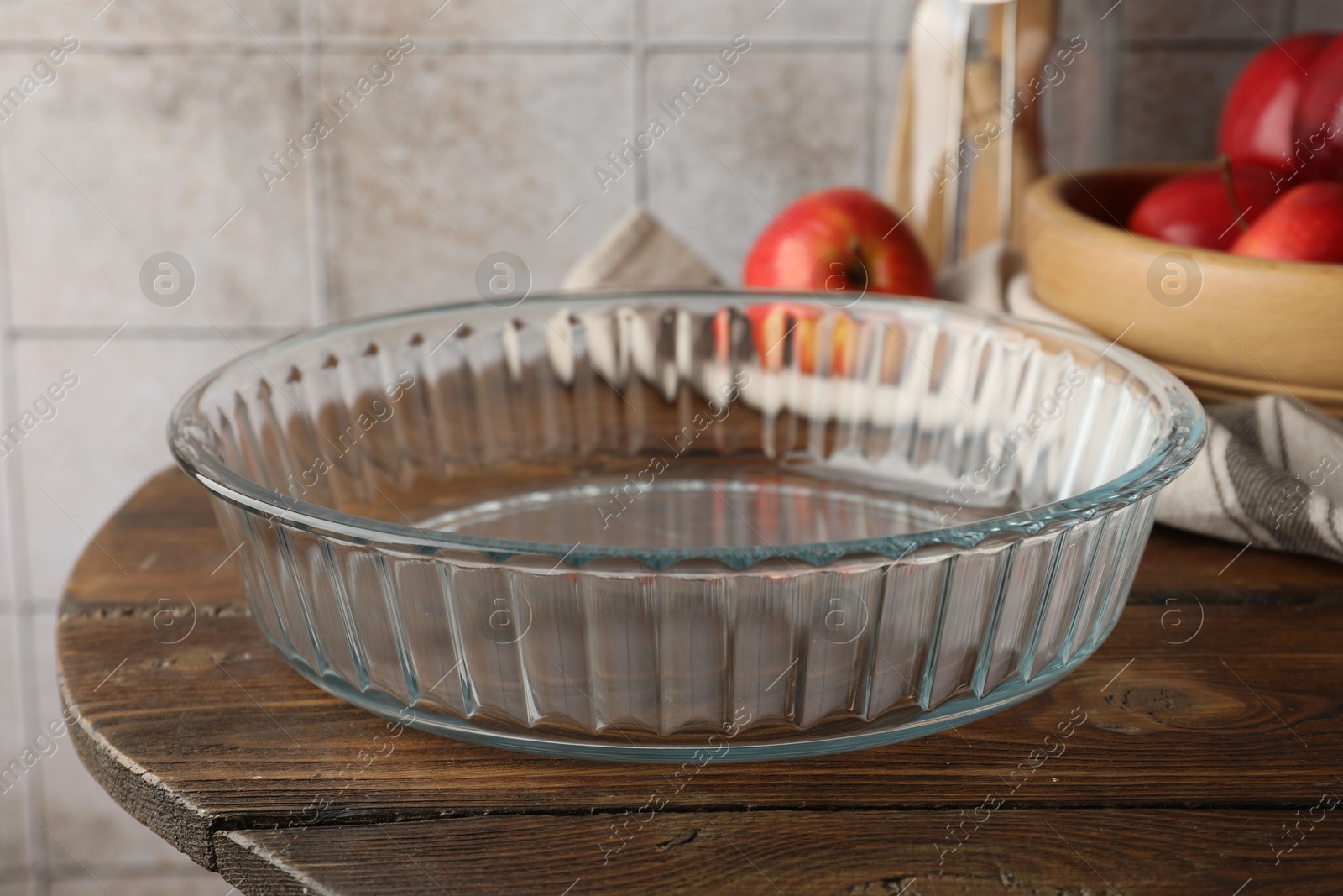 Photo of Glass casserole and apples on wooden table, closeup