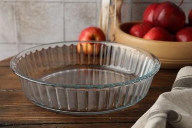 Photo of Glass casserole and apples on wooden table, closeup