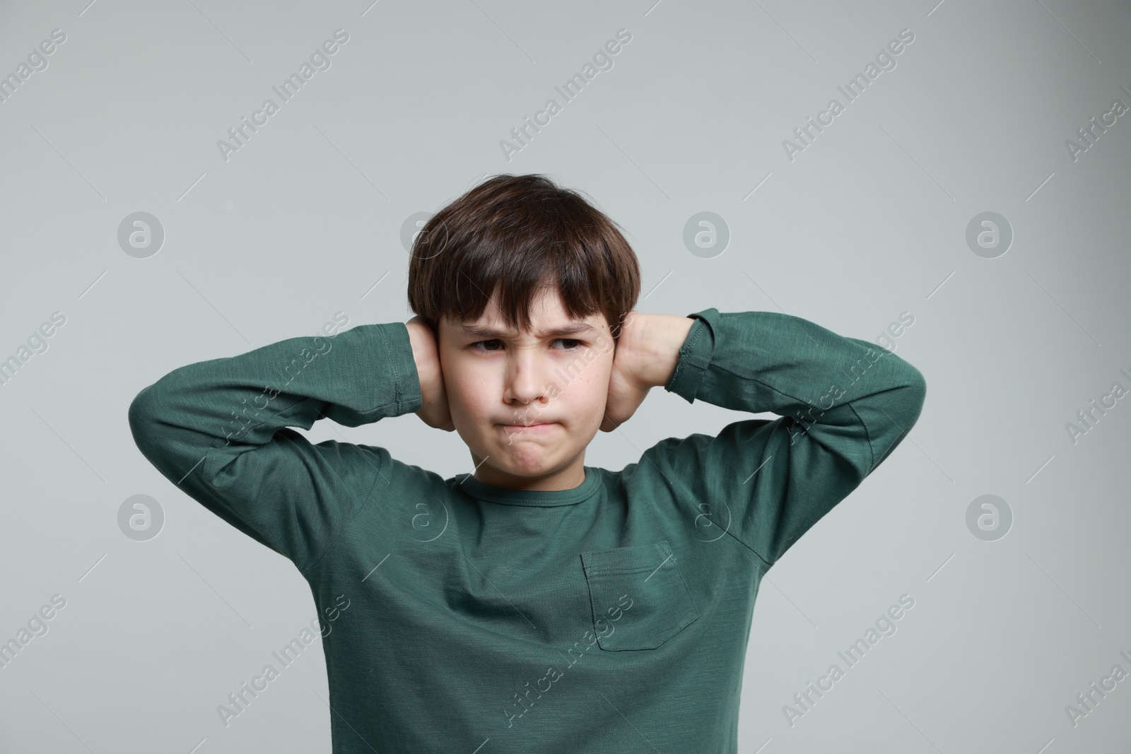 Photo of Annoyed boy covering his ears due to loud sound on grey background