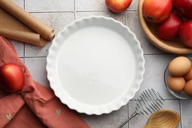 Photo of Ceramic casserole, different cooking utensils, apples and eggs on tiled table, flat lay