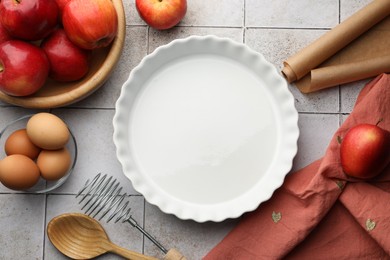 Photo of Ceramic casserole, different cooking utensils, apples and eggs on tiled table, flat lay