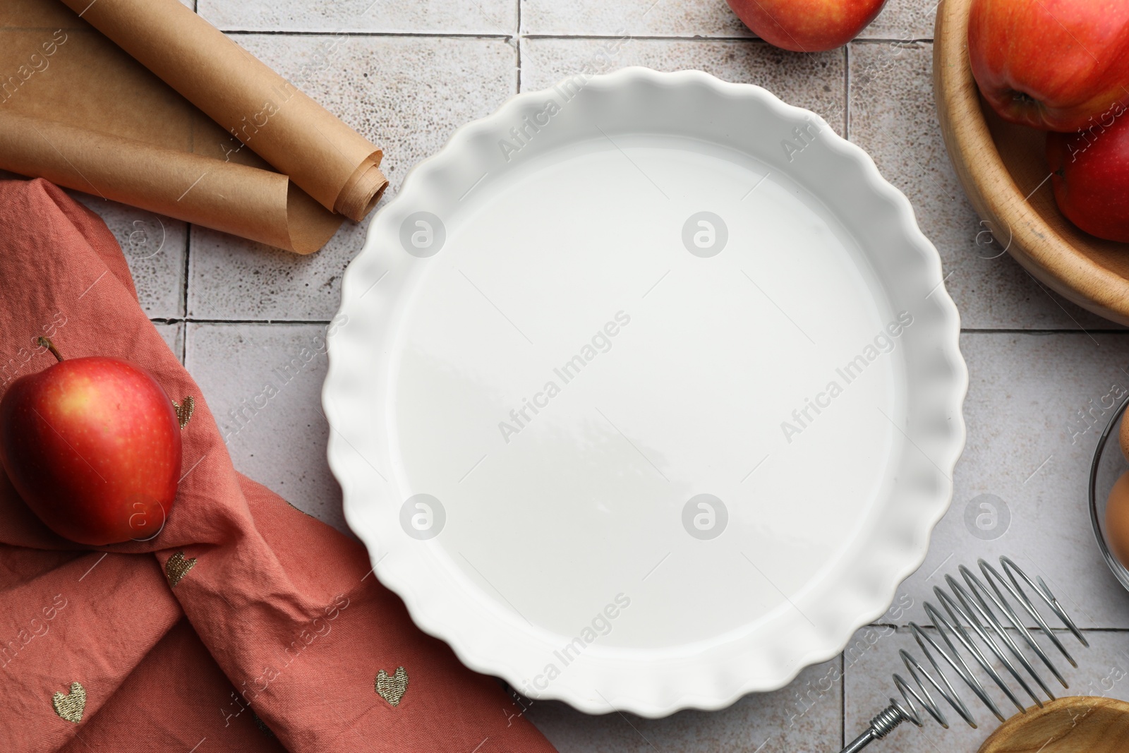 Photo of Ceramic casserole, different cooking utensils, apples and eggs on tiled table, flat lay