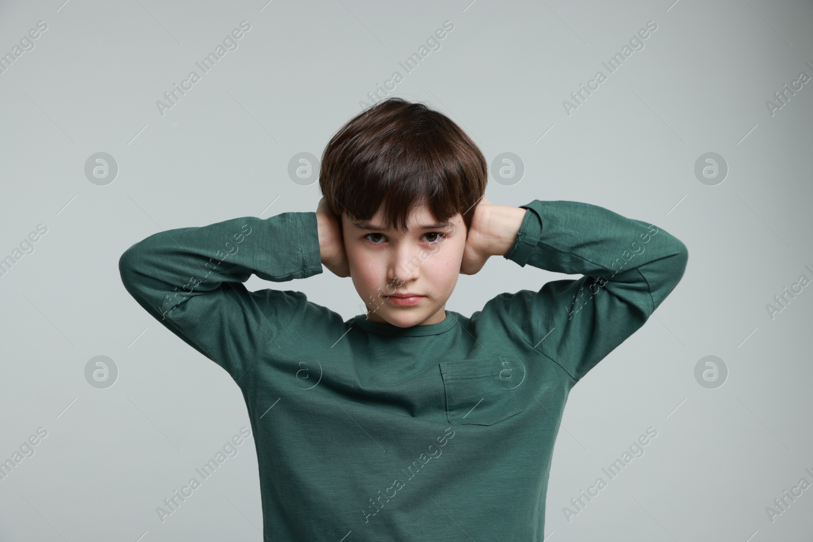 Photo of Annoyed boy covering his ears due to loud sound on grey background