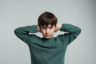 Photo of Annoyed boy covering his ears due to loud sound on grey background