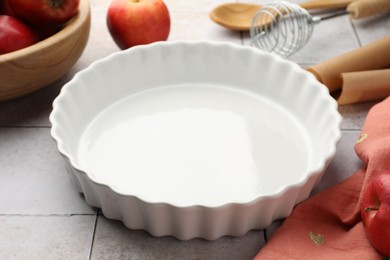 Photo of Ceramic casserole, different cooking utensils and apples on light tiled table, closeup